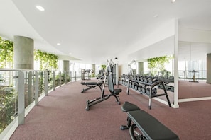 A modern gym with exercise equipment, weight racks, and a bench. - London Skyline 1BR with Rooftop, Gym & Shard Views (Greater London)