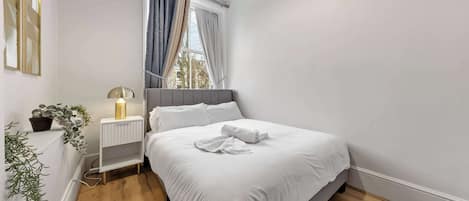 A bedroom with a bed, bedside lamp, and a window with curtains.
