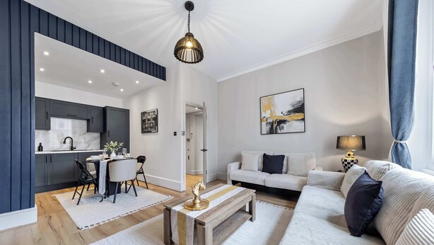 A modern living room with a sofa, coffee table, and a dining area with a table and chairs. - Cinematic Slice of HARRODS for 6 Hideaway Steps from Station (Greater London)