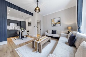 A modern living room with a sofa, coffee table, and a dining area with a table and chairs. - Cinematic Slice of HARRODS for 6 Hideaway Steps from Station (Greater London)