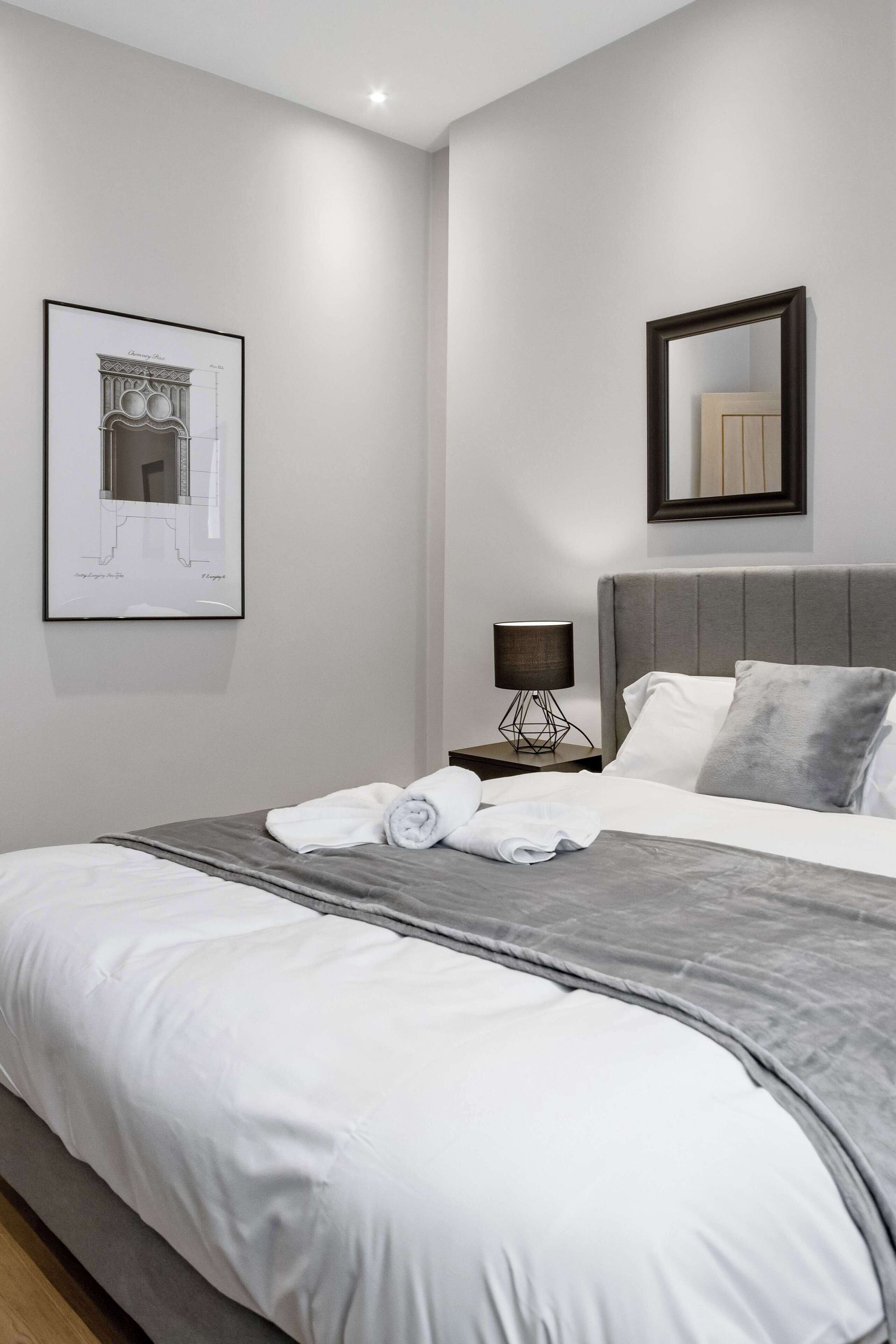 Une chambre à coucher moderne avec un grand lit, une table de chevet avec une lampe et un plan architectural encadré accroché au mur.