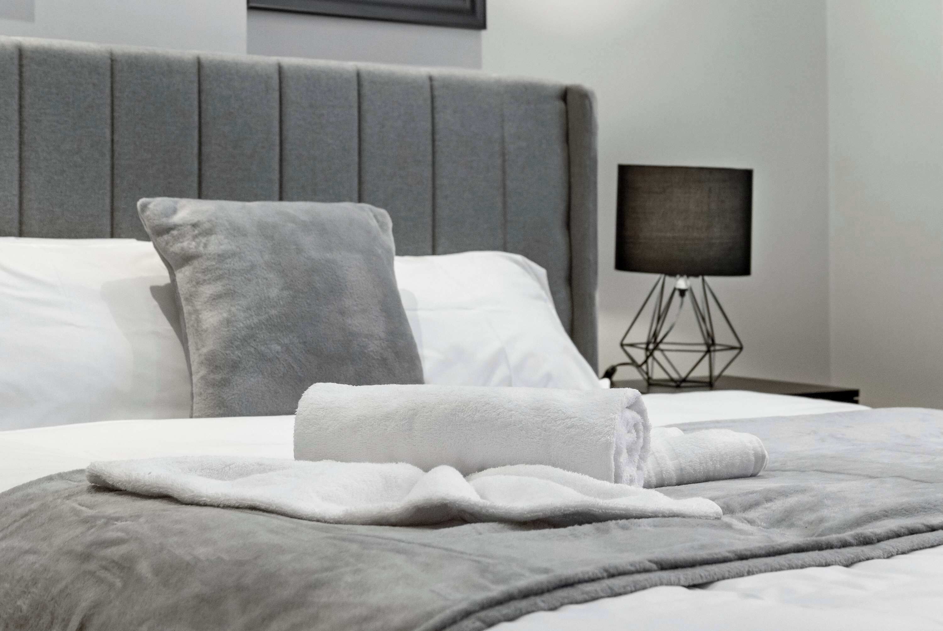 A neatly made bed with a grey headboard, white pillows, and a grey throw blanket.