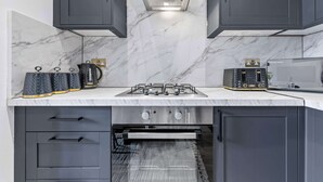 A modern kitchen with grey cabinets, a marble backsplash, a gas stove, and a built-in oven. - Cinematic Slice of HARRODS for 6 Hideaway Steps from Station (Greater London)