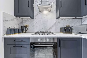 A modern kitchen with grey cabinets, a marble backsplash, a gas stove, and a built-in oven. - Cinematic Slice of HARRODS for 6 Hideaway Steps from Station (Greater London)
