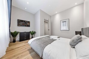 A modern bedroom with a large bed, a black dresser, two potted plants, a wall-mounted TV, and a framed picture. - Cinematic Slice of HARRODS for 6 Hideaway Steps from Station (Greater London)