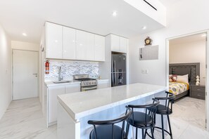 A modern kitchen with white cabinets, a marble countertop, and a central island with bar stools. - Luxury Condo With Shared Gym, Rooftop Pool, and Centrally Located (Cabo San Lucas)