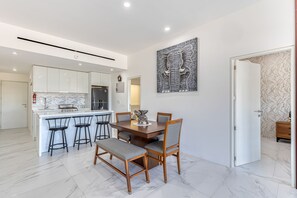 A modern kitchen with white cabinets, a marble countertop, and a dining area with a wooden table and chairs. - Luxury Condo With Shared Gym, Rooftop Pool, and Centrally Located (Cabo San Lucas)