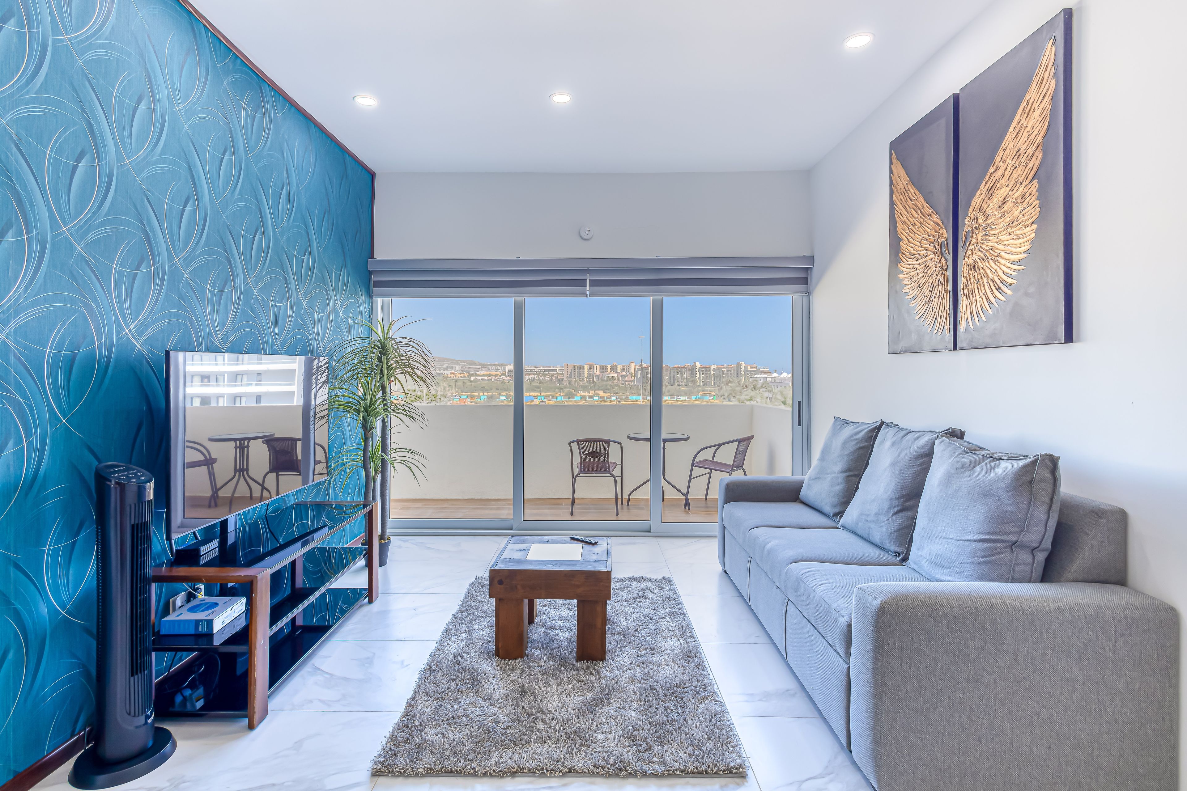 A modern living room with a grey sofa, a wooden coffee table, and a blue patterned wall.