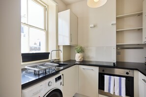 A compact kitchen with a washing machine, a sink, and a small oven. - Olive Velvet & Marble - South Kensington (London)