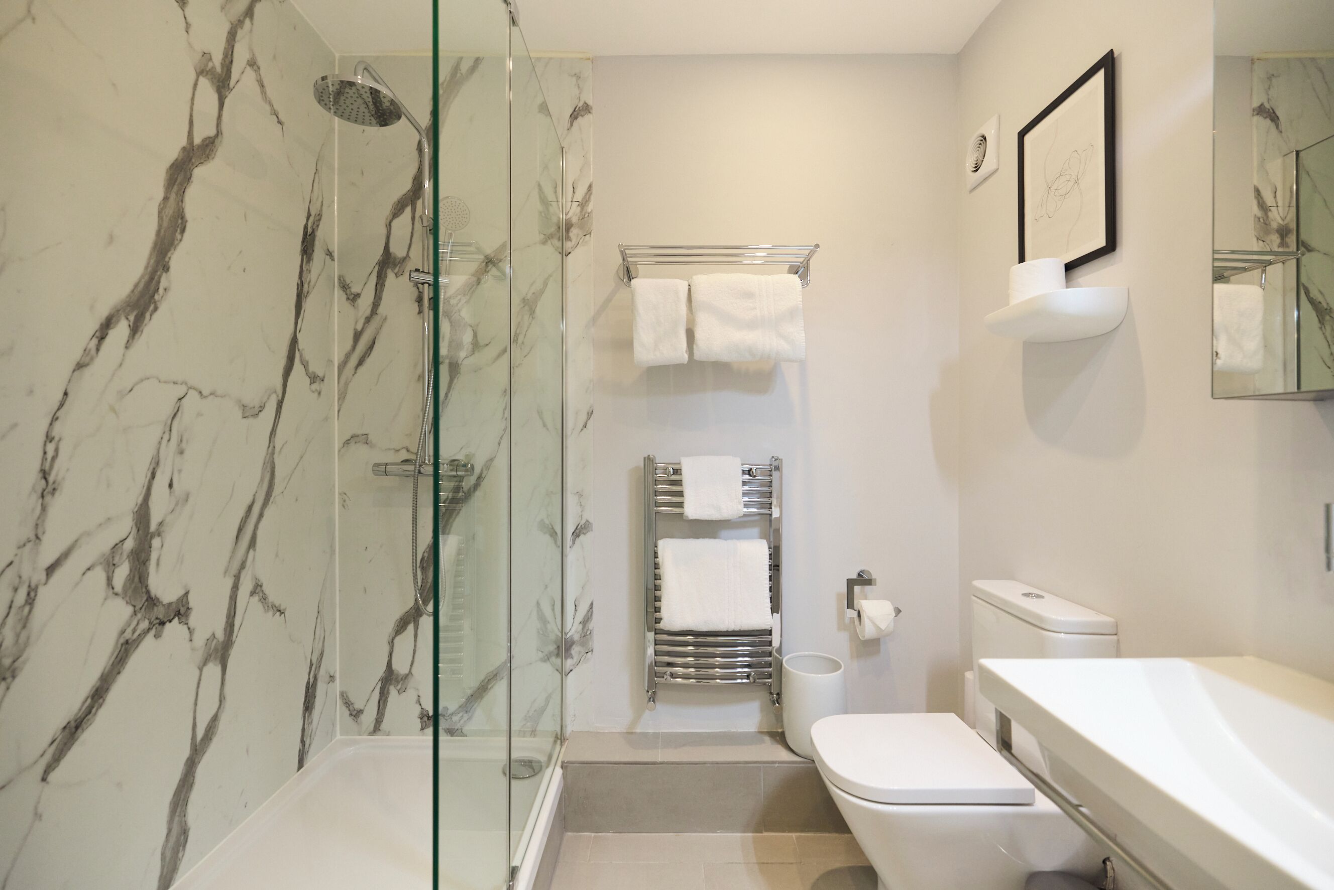 A bathroom with a glass shower enclosure, a toilet, a sink, and a towel rack.