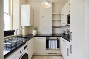 A compact kitchen with a built-in oven, a dishwasher, and a sink. - Olive Velvet & Marble - South Kensington (London)