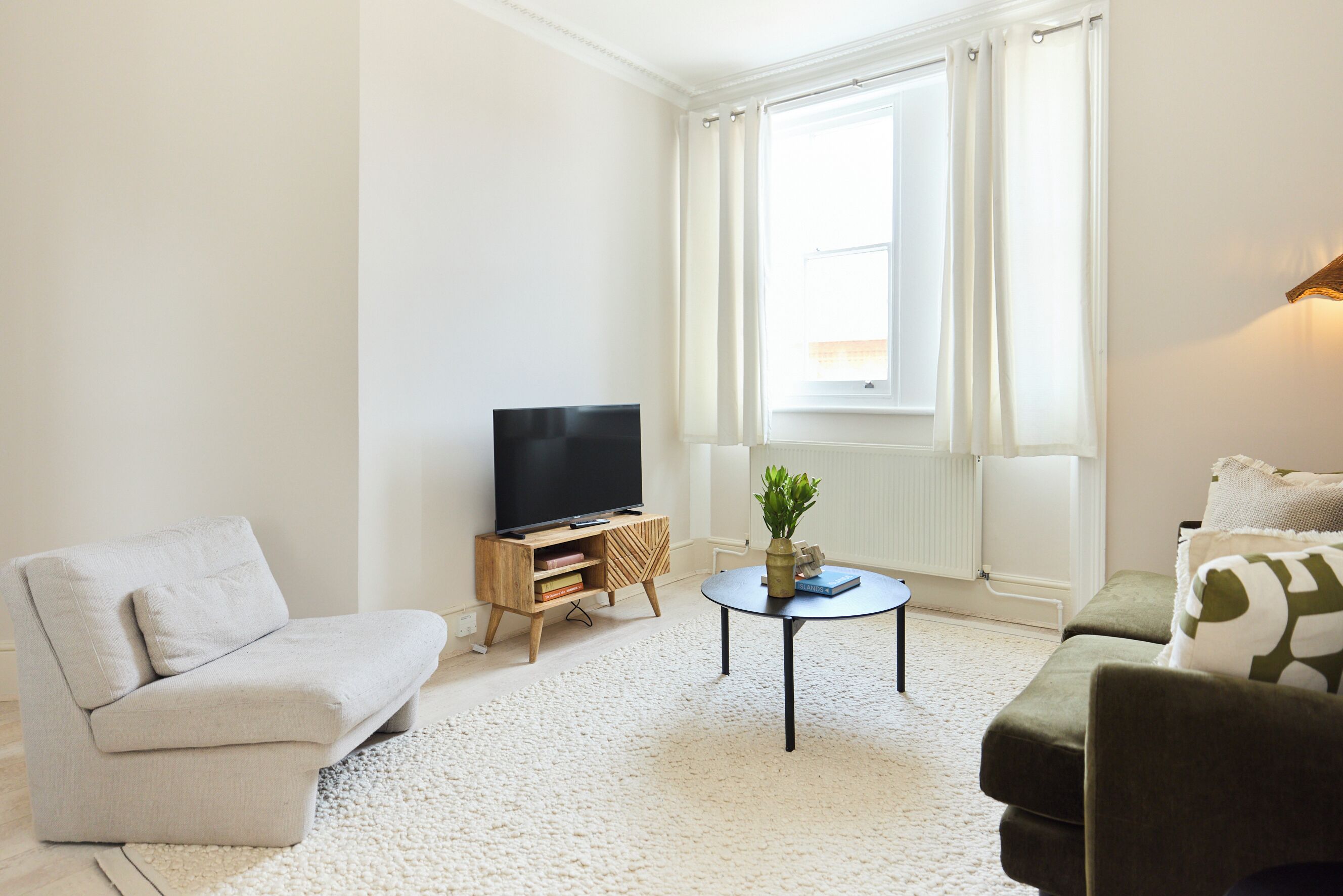 Sala de estar com sofá, mesa de centro, rack para TV e janela com cortinas.