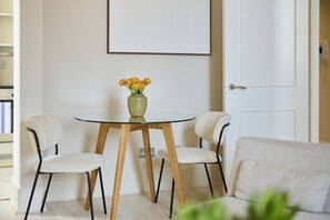 A dining area with a glass table, two chairs, a vase with flowers, and a door in the background. - Olive Velvet & Marble - South Kensington (London)