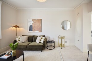 A modern living room with a sofa, a round mirror, a floor lamp, and a piece of abstract art on the wall. - Olive Velvet & Marble - South Kensington (London)