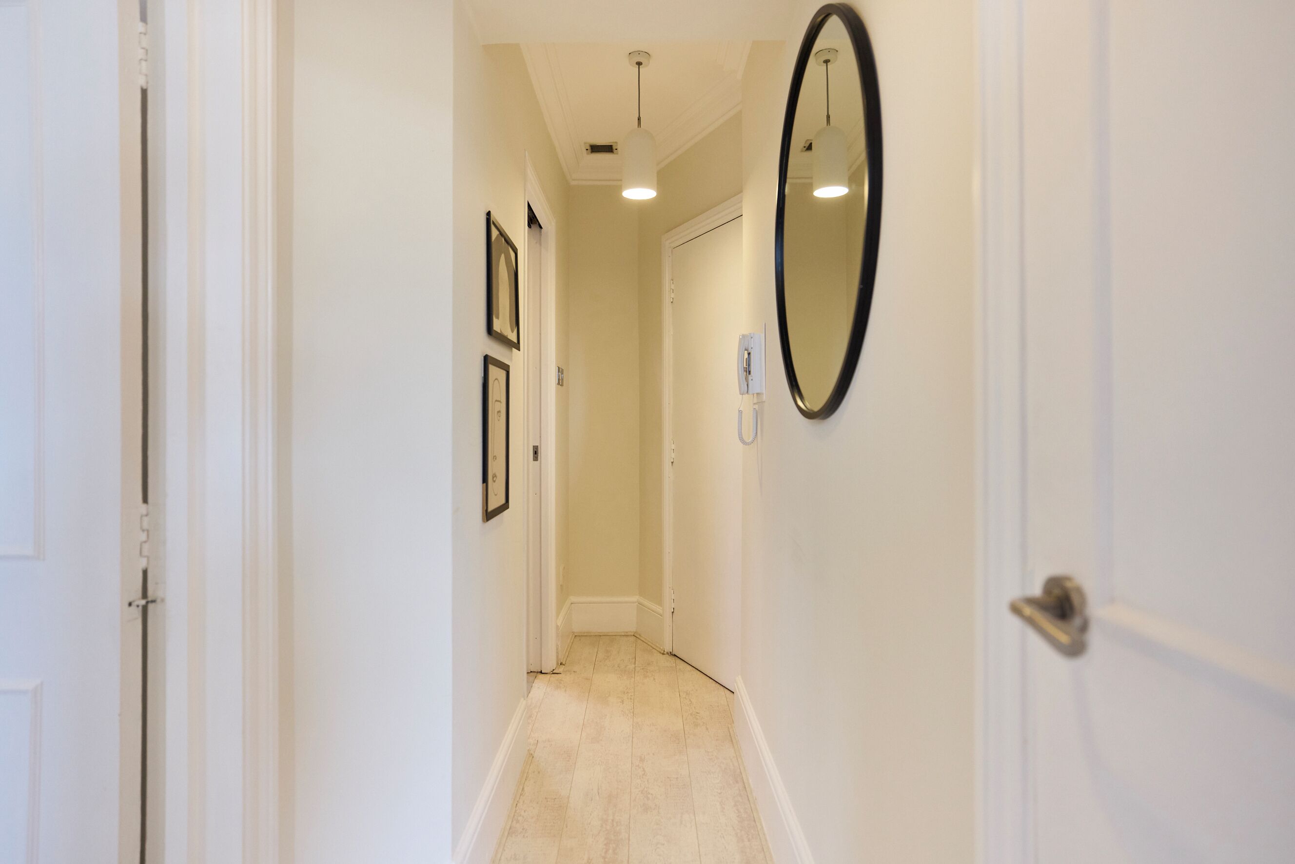 A narrow hallway with white walls, a light-colored floor, and a door at the end.