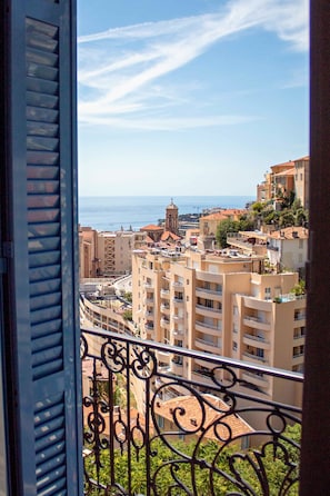 Un balcón con vista a un paisaje urbano costero, que incluye edificios y una iglesia.