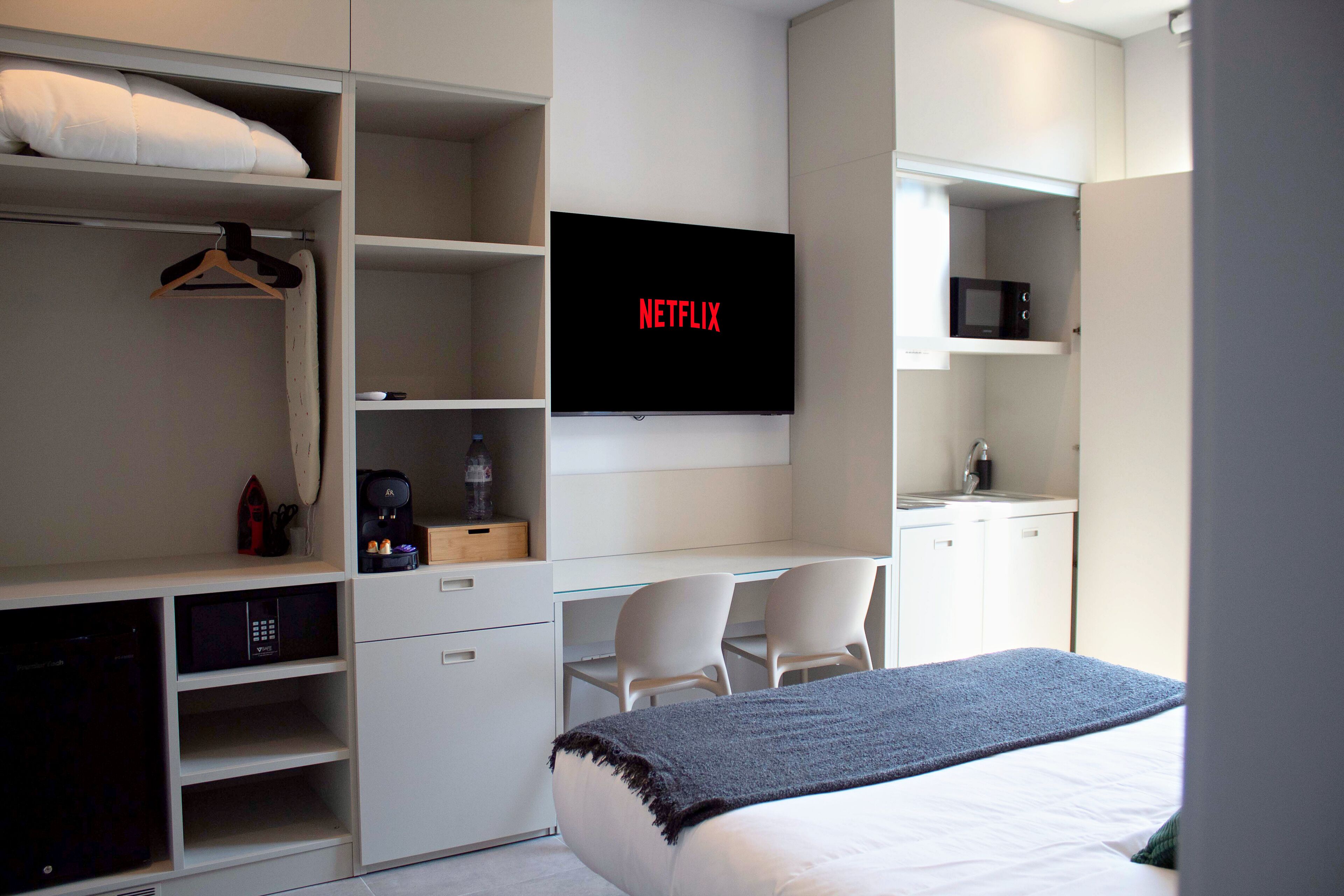 Une chambre d’hôtel moderne équipée d’un lit, d’un téléviseur fixé au mur, d’un bureau avec une chaise et d’une armoire.