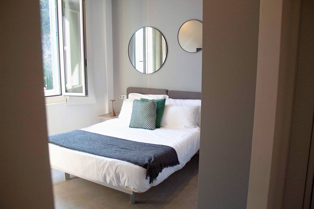A bedroom with a bed, a window, and two wall-mounted mirrors.