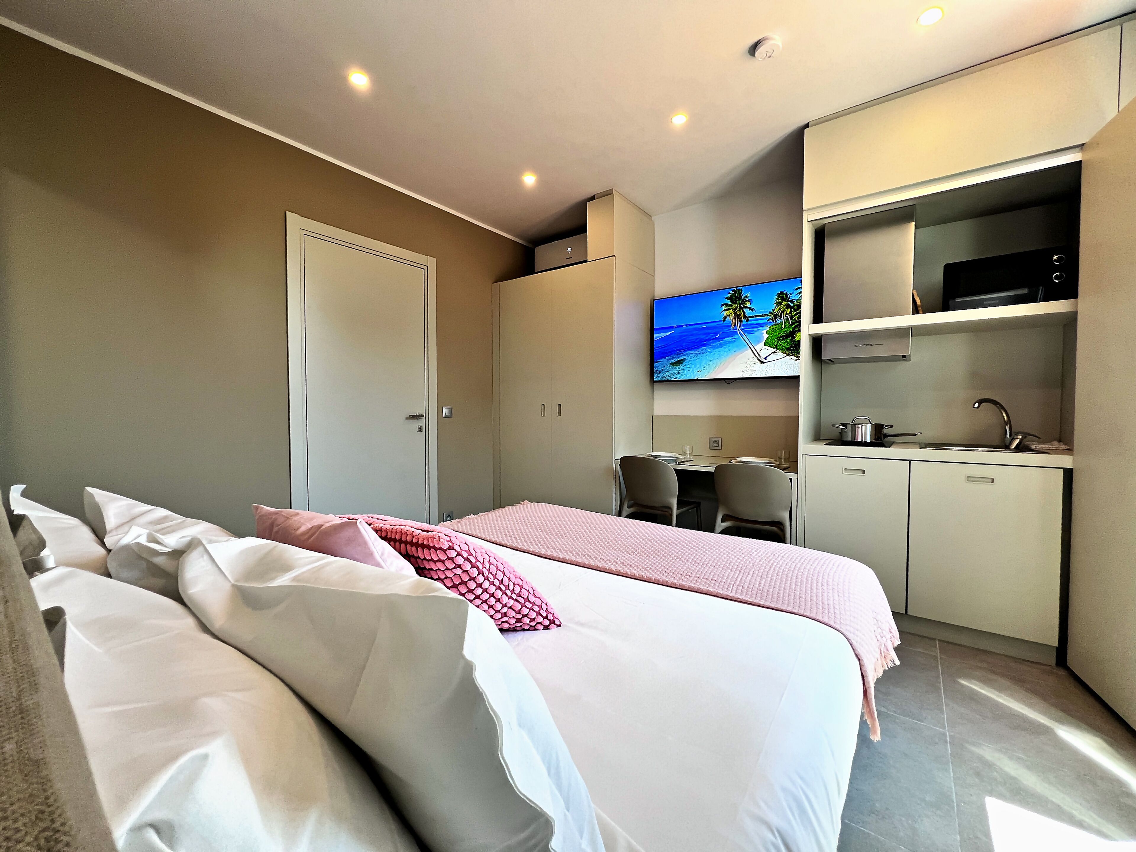 Ein Hotelzimmer mit Bett, Schreibtisch, Fernseher und einer Küchenzeile.