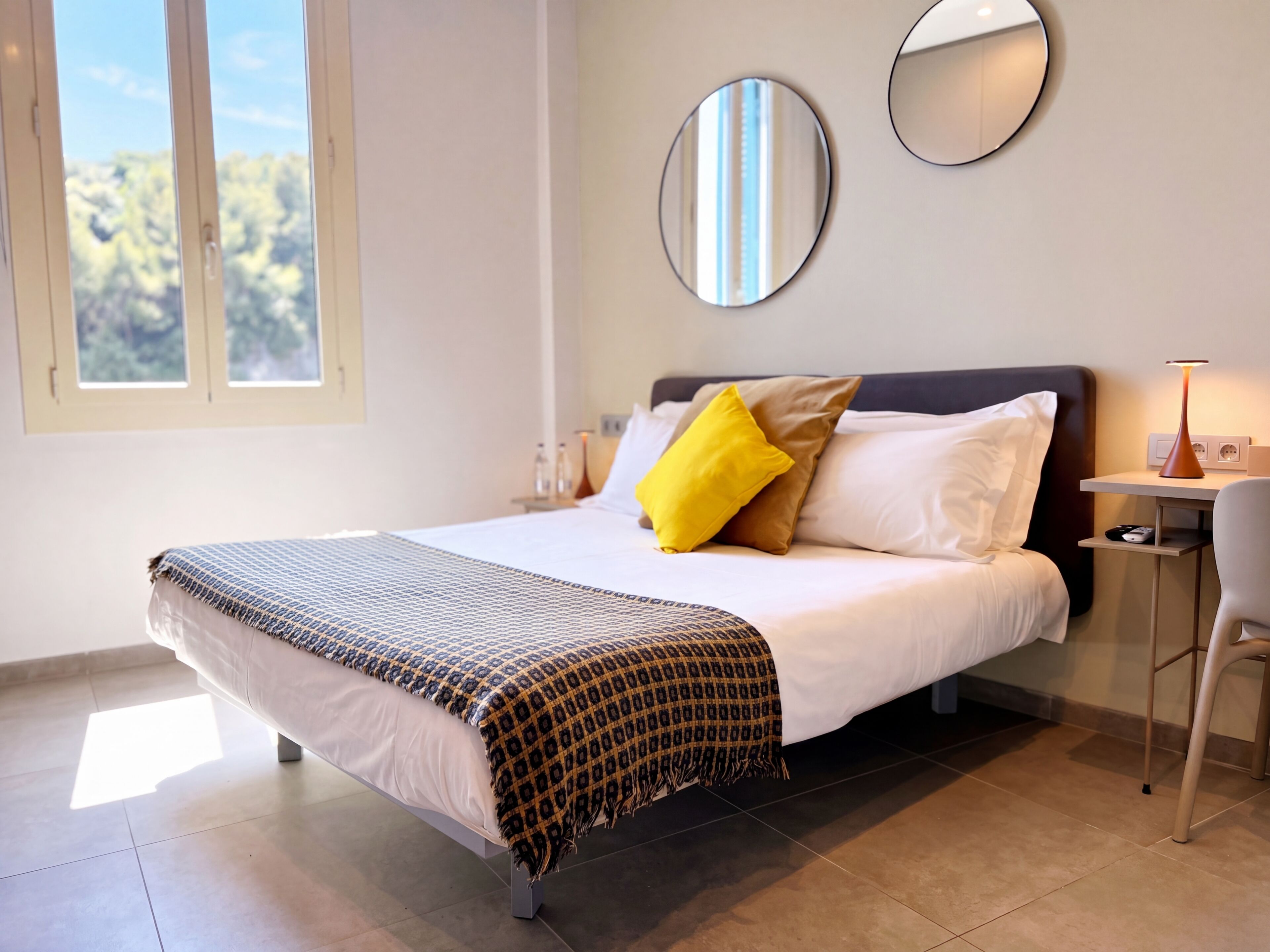A neatly made bed with patterned bedding, a bedside table with a lamp, and two wall mirrors.