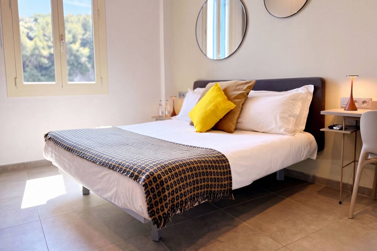 A neatly made bed with patterned bedding, a bedside table with a lamp, and two wall mirrors.