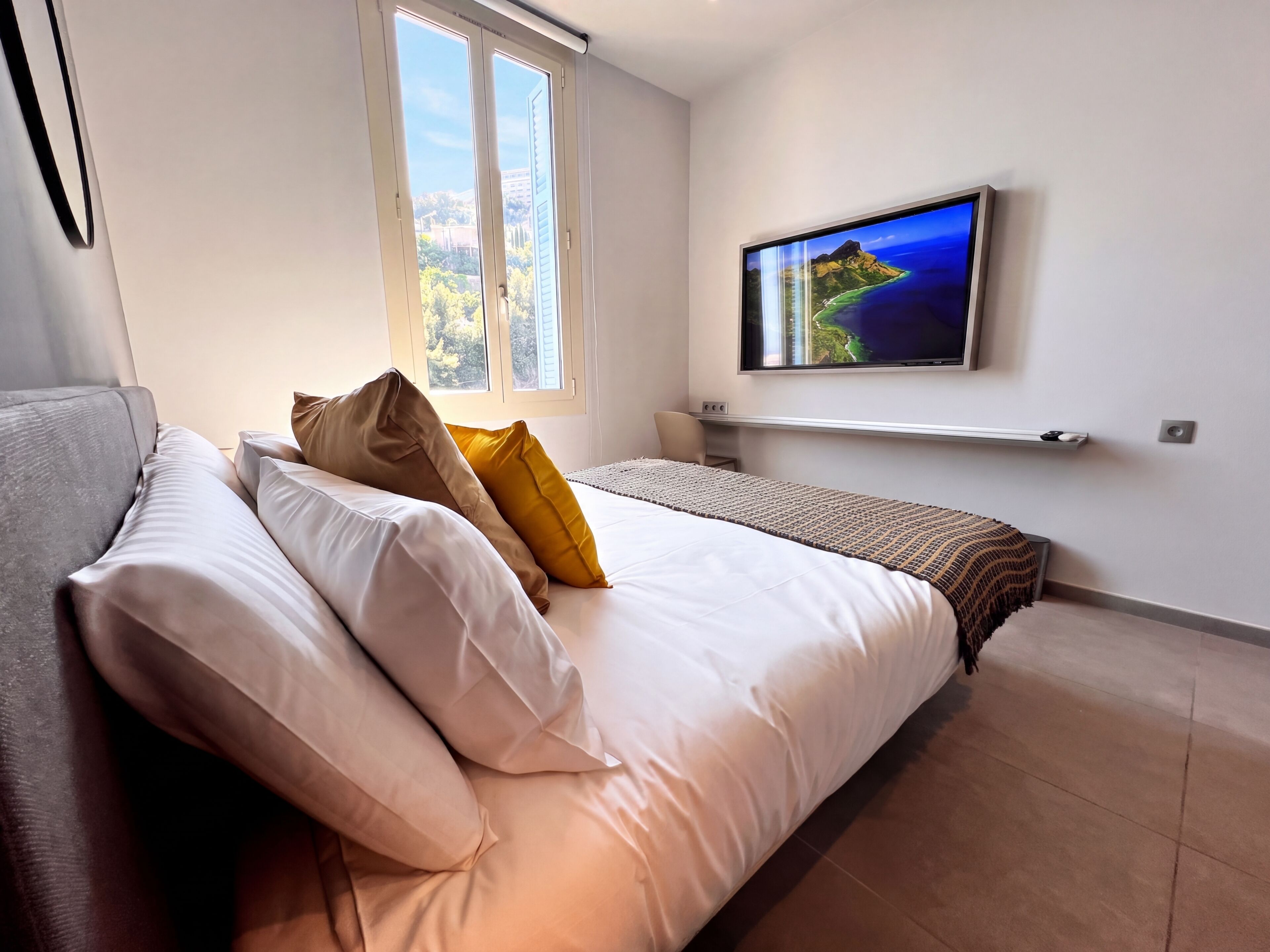 Une chambre à coucher avec un lit, des oreillers, une télévision, une fenêtre et une vue sur un paysage.