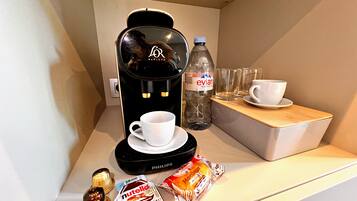 A coffee machine, a bottle of Evian water, two glasses, a cup, a Nutella bar, and a chocolate bar on a counter.