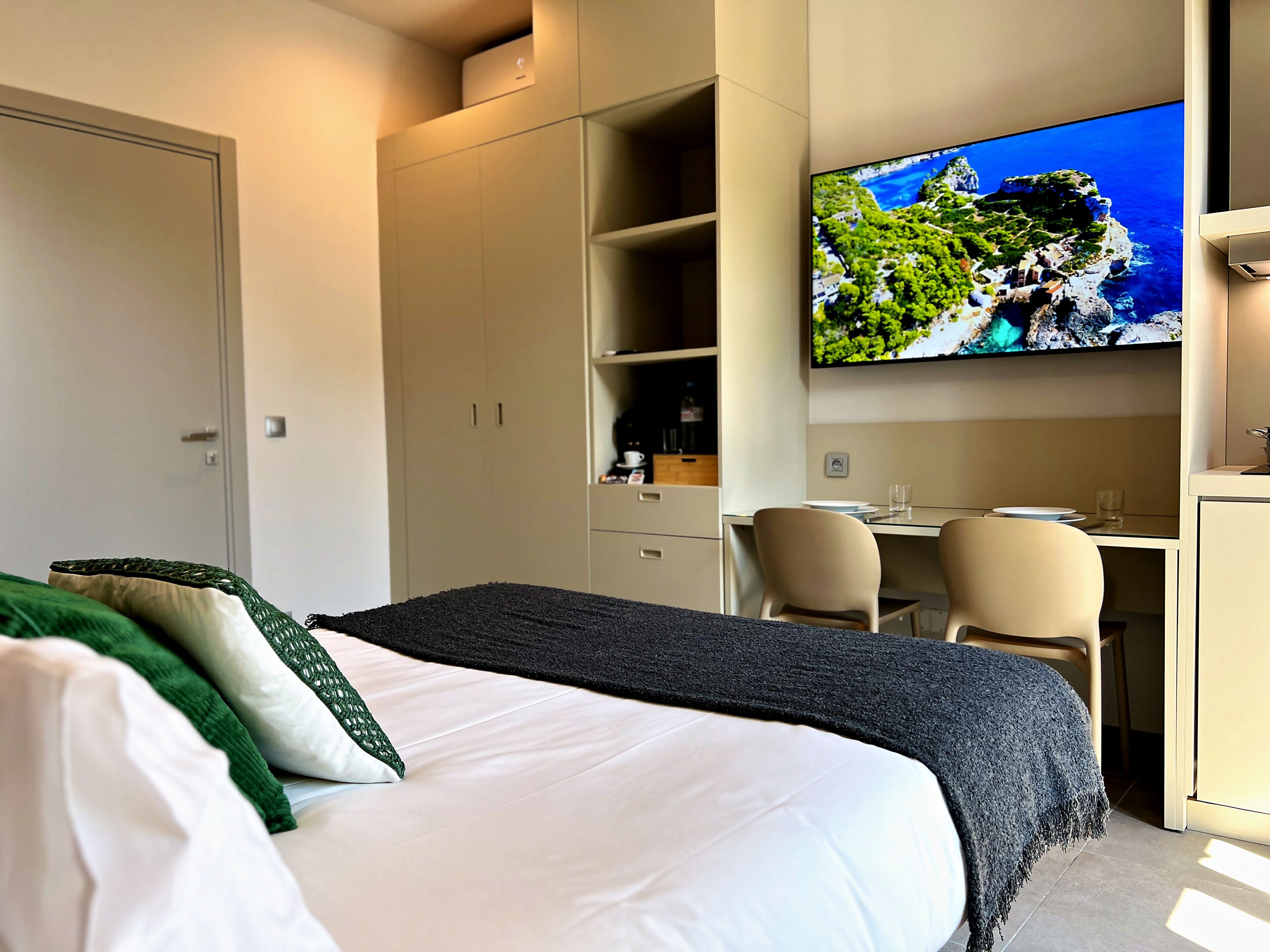 A hotel room with a bed, a desk, a chair, a television, and a wardrobe.