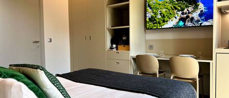 A hotel room with a bed, a desk, a chair, a television, and a wardrobe.
