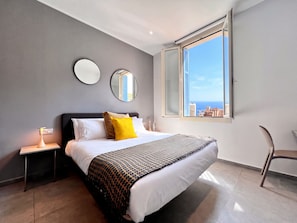 Un dormitorio moderno con cama, mesitas de noche, una silla y un ventanal con vistas a la ciudad.