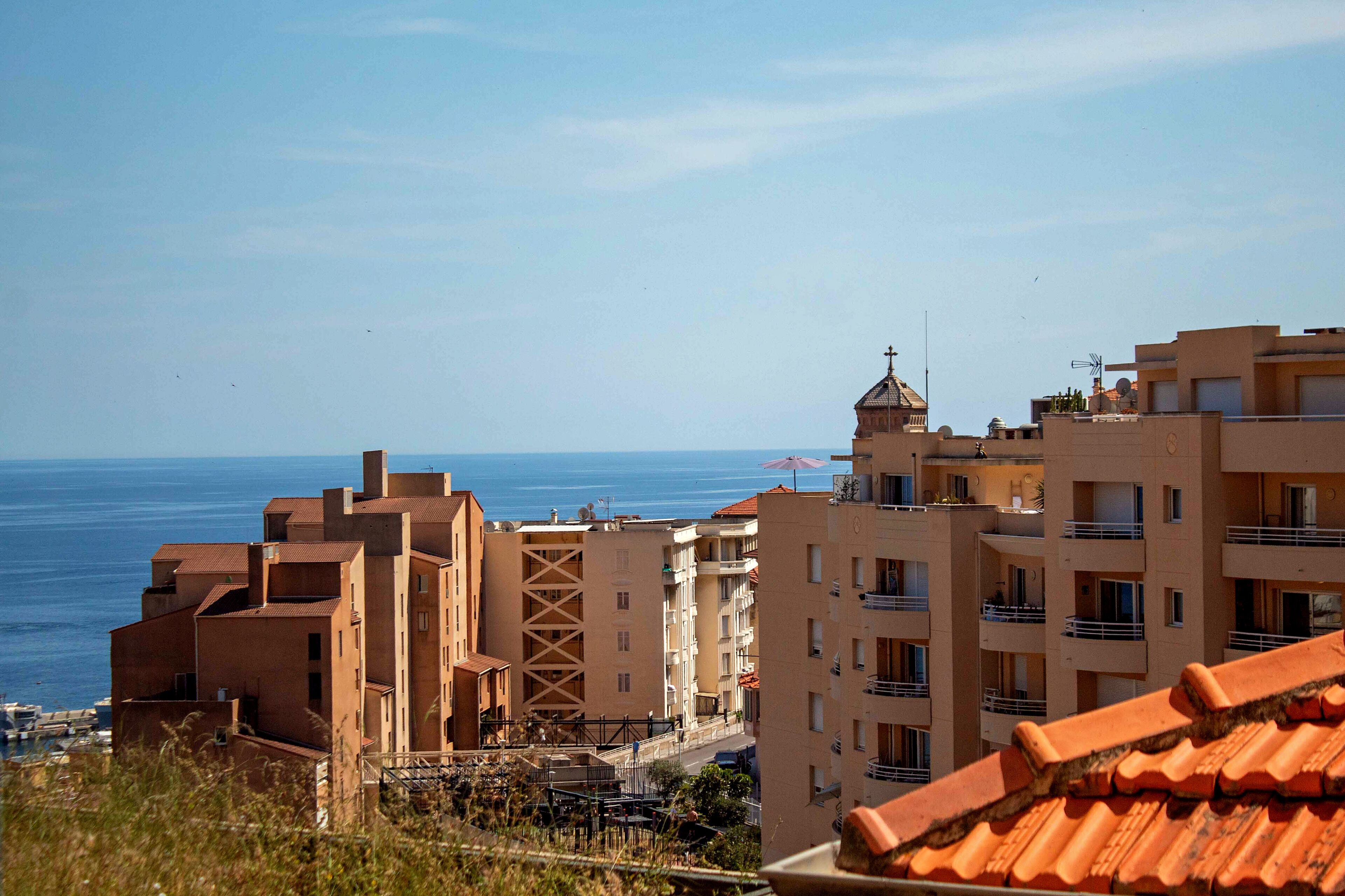 A coastal residential area with buildings, a view of the sea, and a clear sky.