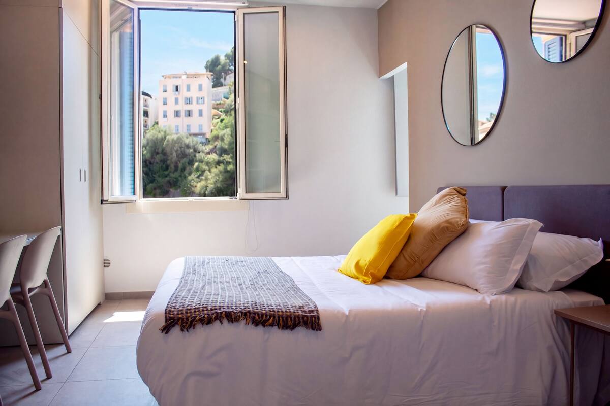 A bedroom with a bed, a chair, a window, and a mirror.