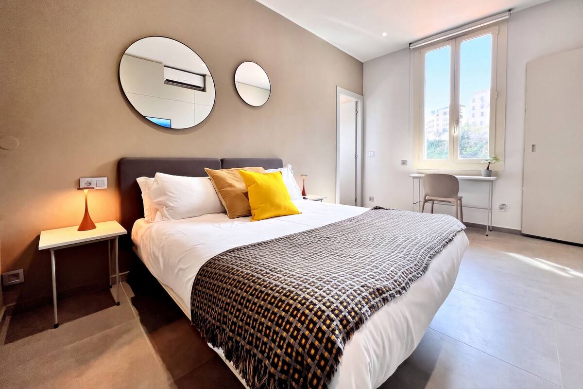 A modern hotel room with a large bed, bedside tables, a desk, and a window with a view.