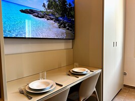 A dining area with a TV displaying a beach scene, a table set with plates and cutlery, and a chair.