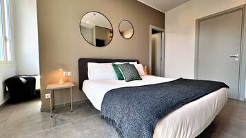 A bedroom with a bed, bedside table, lamp, two wall mirrors, and a wardrobe.