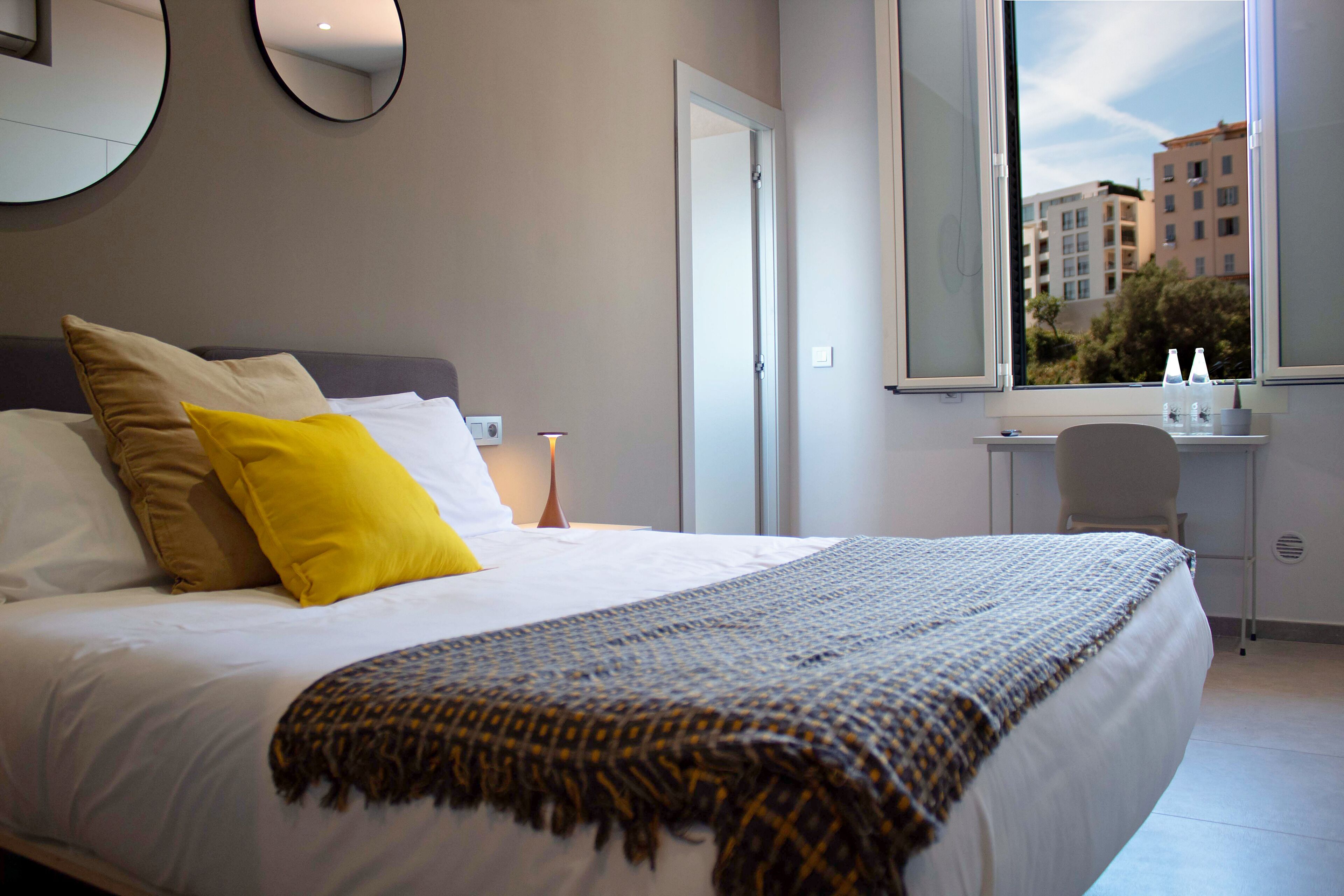 Habitació d'hotel moderna amb un llit gran, una taula de treball i una finestra amb vista a la ciutat.