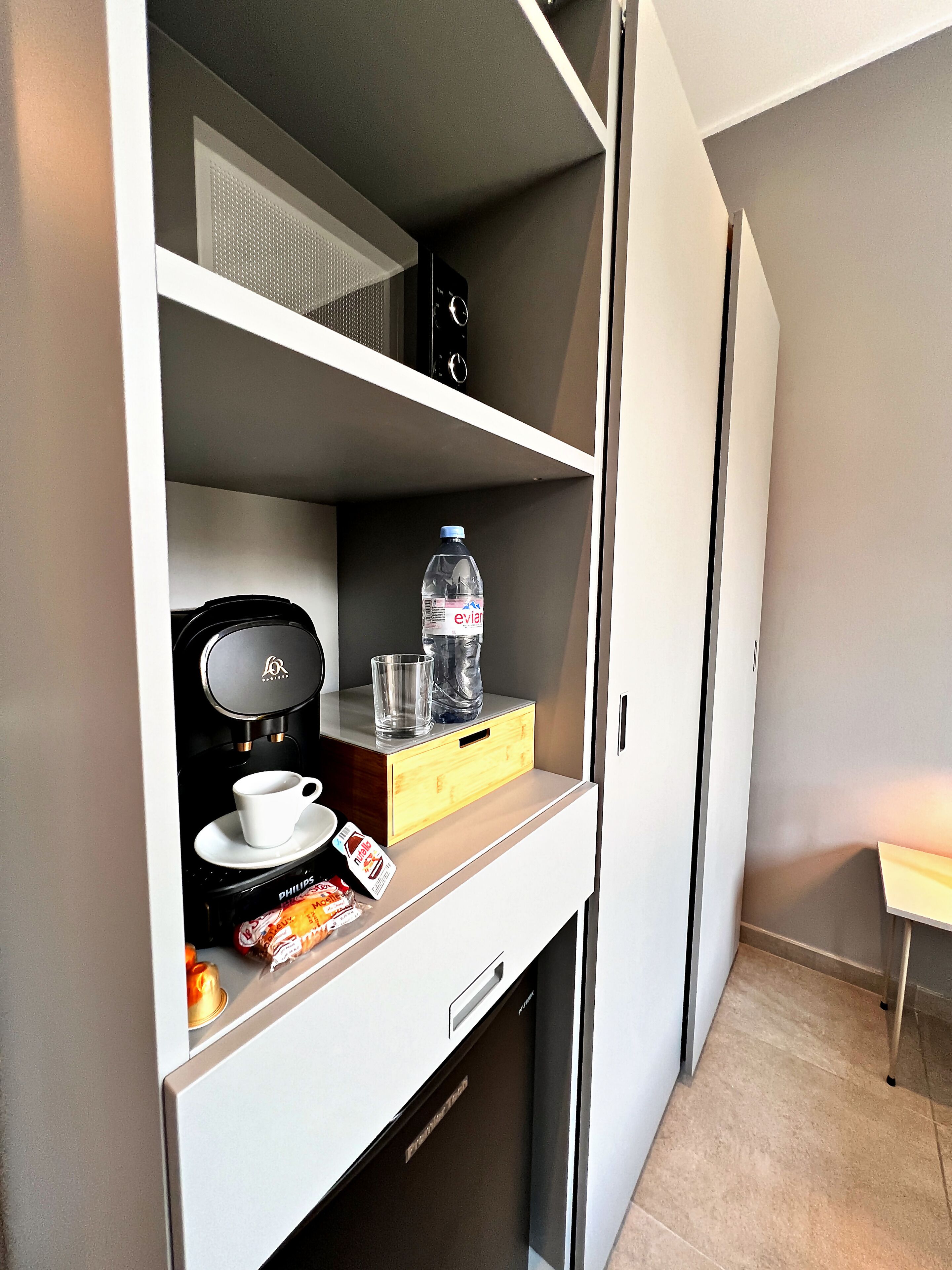 Une petite cuisine équipée comprenant une machine à café, une bouteille d’eau et un verre posés sur le comptoir.