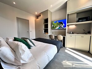 A modern hotel room with a bed, a desk with a TV, a kitchenette, and a wardrobe. - My Residence d'Azur (Beausoleil)