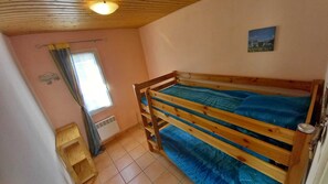 Eine kleine, einfache Unterkunft mit Etagenbett, einem Vorhangfenster, einem Heizkörper und einem Bild an der Wand.
