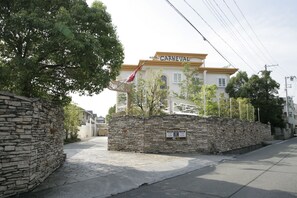 A hotel named 'Hotel Carnaval' with a stone wall entrance, a flag, and a clear sky. - HOTEL CARNEVAL - Adults Only (Himeji)