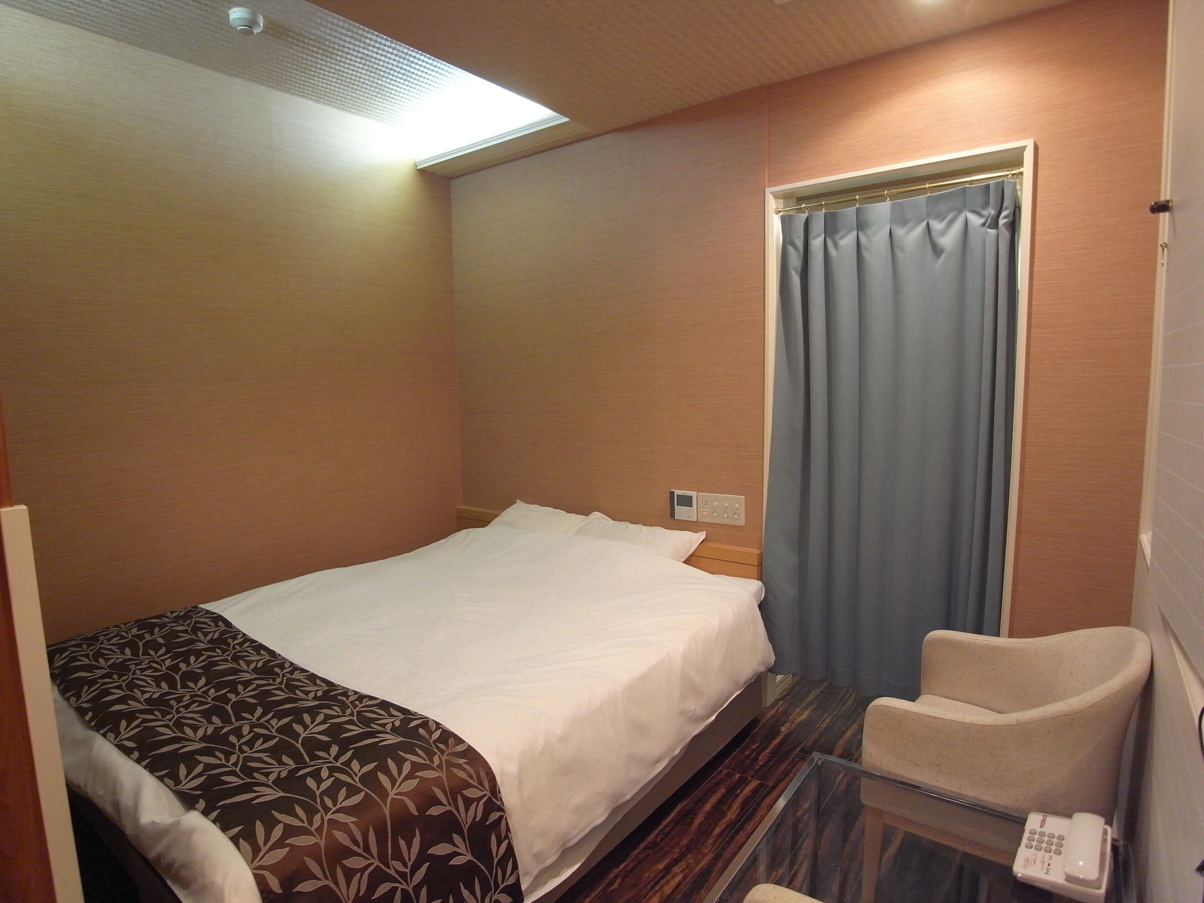 Une chambre d’hôtel avec un lit, une chaise, un téléphone et une fenêtre avec des rideaux.