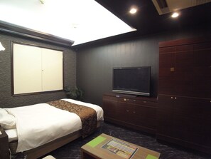 A hotel room with a bed, a television, a wardrobe, and a ceiling light. - HOTEL CARNEVAL - Adults Only (Himeji)