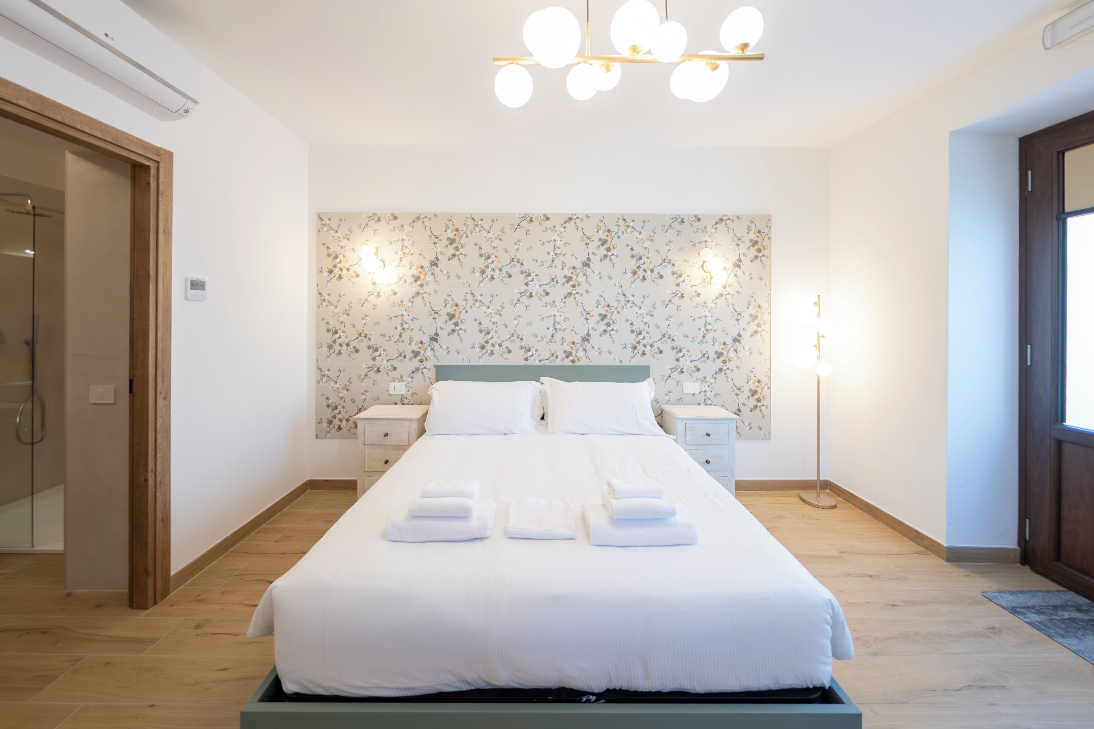 A hotel room with a bed, bedside tables, a wall-mounted light fixture, and a door.. New Farmhouse immersed in the Green at the gates of Rome