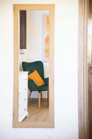 Una habitació amb terra de fusta, una cadira amb fons verd i un coixí taronja, i un moble cec blanc.