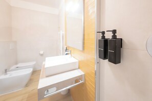 Un bany modern amb un lavabo blanc, un mirall i dos dispensadors de xampú negres fixats a la paret.