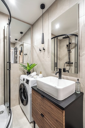 A modern bathroom with a washing machine, a sink, a mirror, and a shower. - RentPlanet - Apartamenty Dyrekcyjna (Katowice)