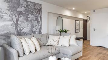 A modern living room with a grey sofa, a large wall mural, a mirror, and a plant.