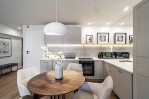 A modern kitchen with a marble countertop, built-in oven, and a dining area with a round wooden table and chairs. - RentPlanet - Apartamenty Dyrekcyjna (Katowice)