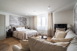 A modern hotel room with a large bed, a sofa, a TV, and a painting on the wall. - RentPlanet - Apartamenty Dyrekcyjna (Katowice)