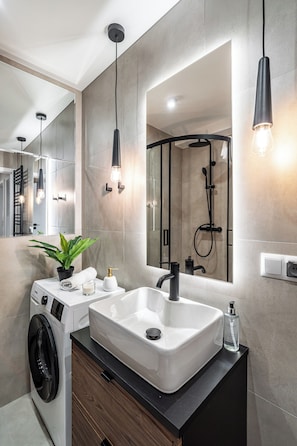 A modern bathroom with a built-in washing machine, a sink, and a shower area. - RentPlanet - Apartamenty Dyrekcyjna (Katowice)